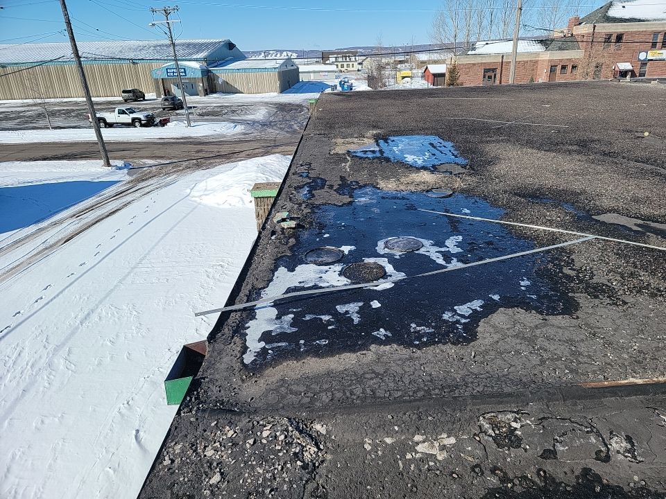 Severely damaged commercial flat roof with standing water and membrane failure in winter.