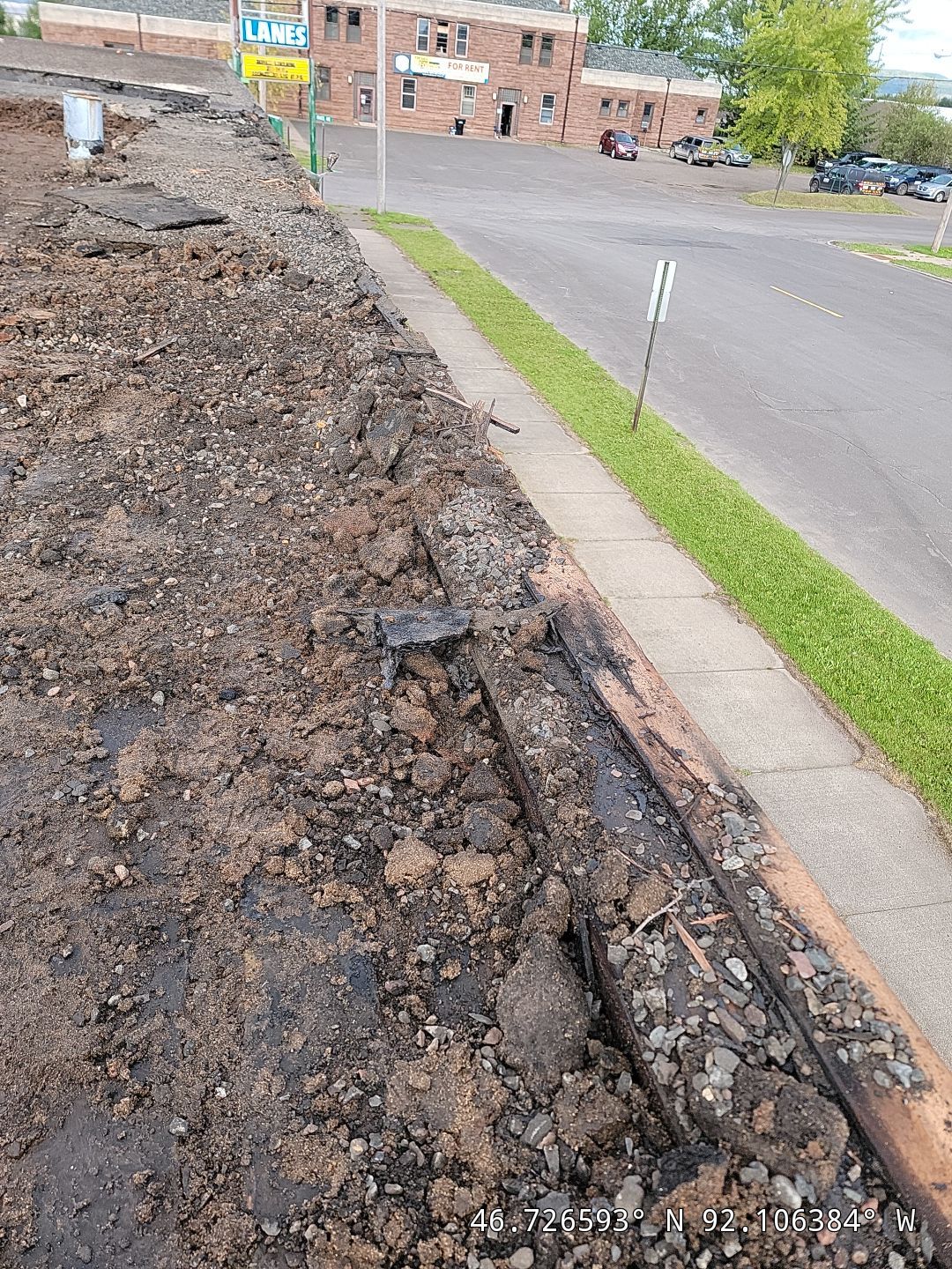 Severely deteriorated commercial flat roof edge during tear-off showing failed gravel ballast and roofing layers.