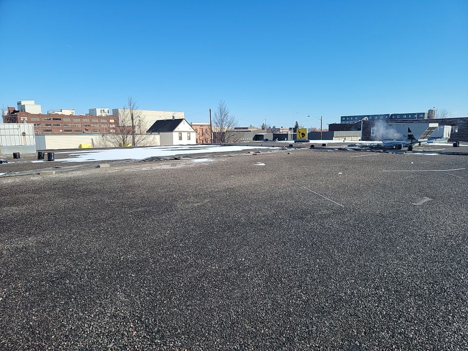 Aged commercial gravel ballast flat roof during inspection.