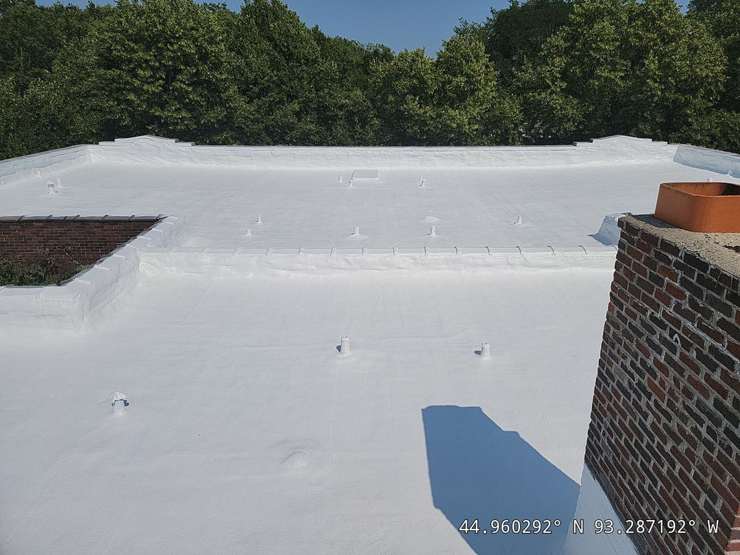 Completed white coating flat roof installation with brick chimney flashing detail
