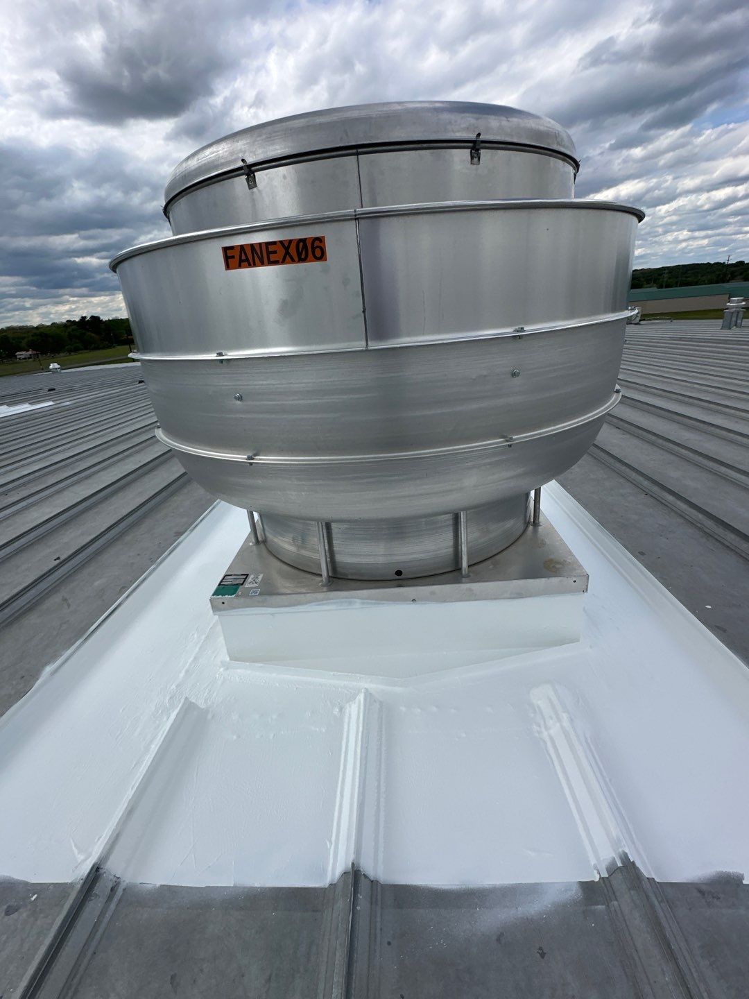 Inspected industrial exhaust fan with white liquid coating on the roof and clean flashing detail