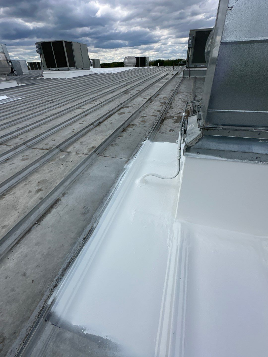 Liquid roof coating applied at seam between metal and flat roof sections