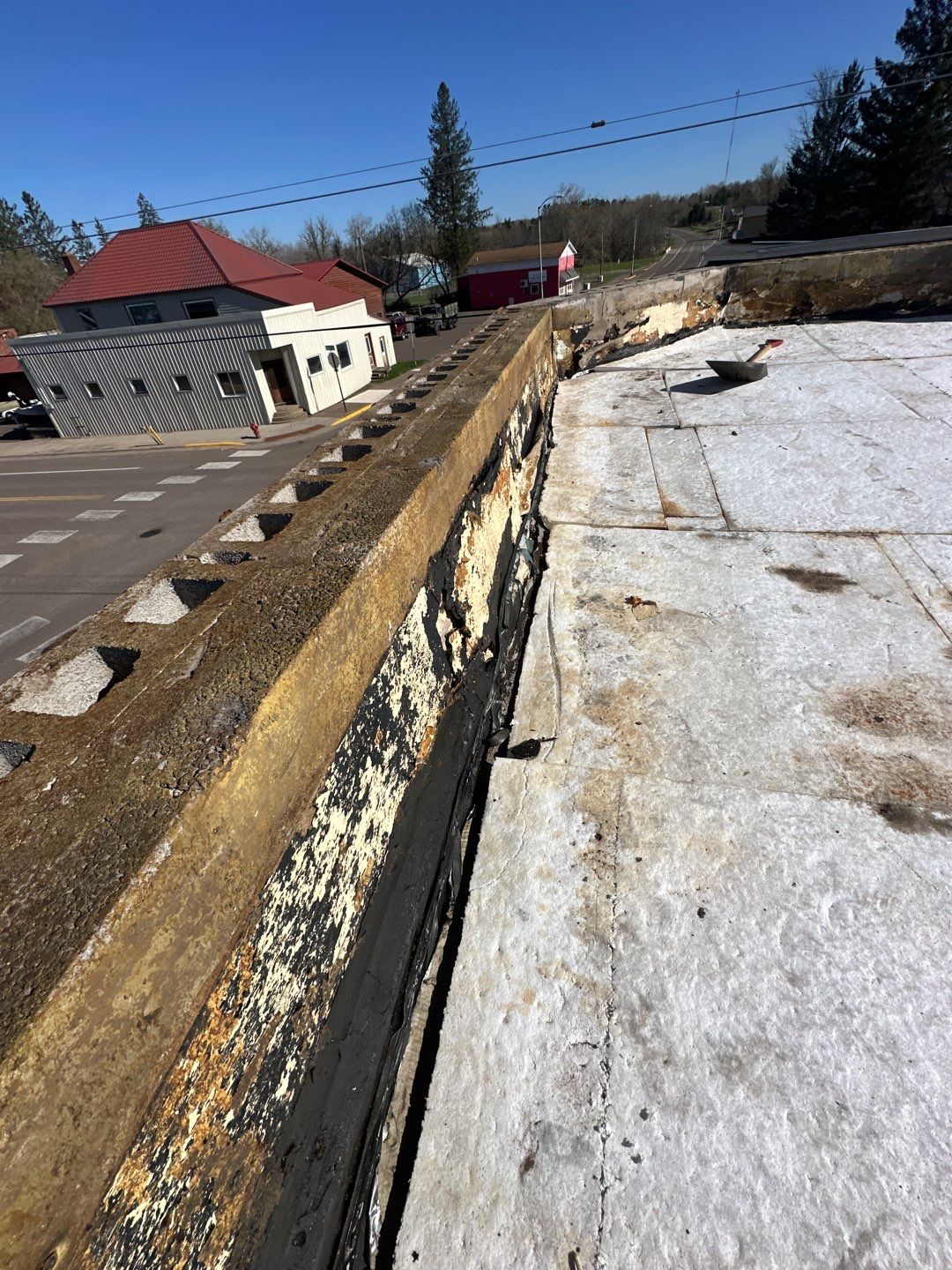 Severely deteriorated flat roof edge with failed parapet flashing and crumbling membrane
