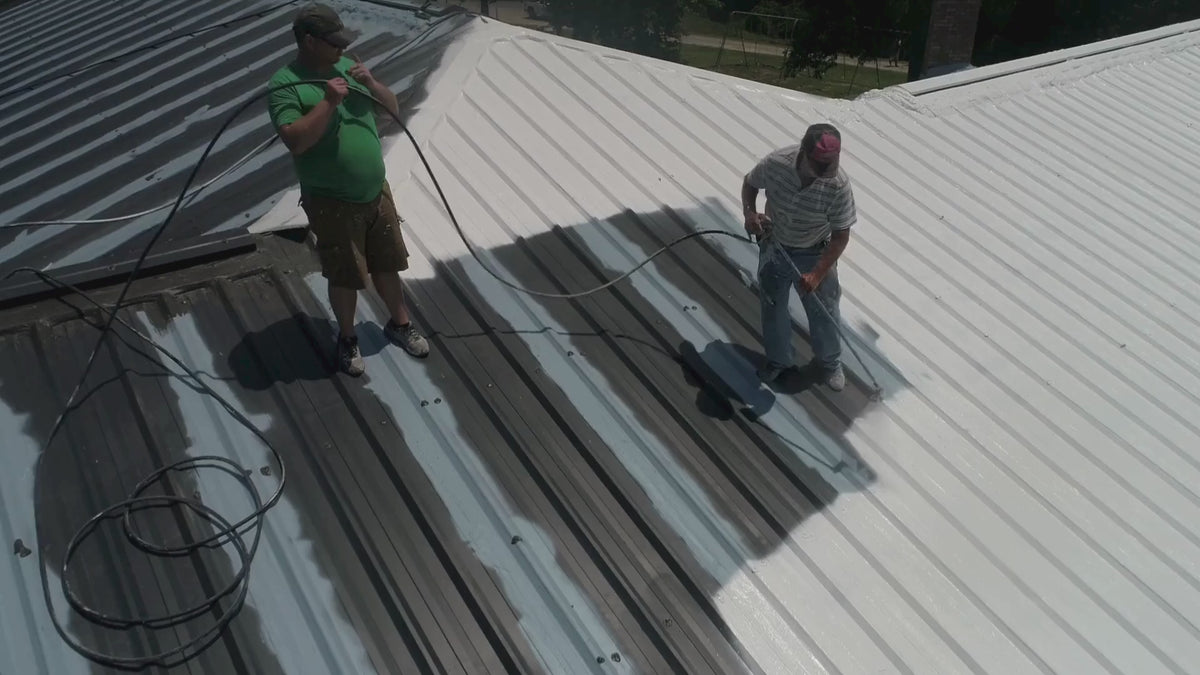 Arial view of two workers working on the roof, coating it with white paint.