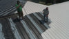 Arial view of two workers working on the roof, coating it with white paint.
