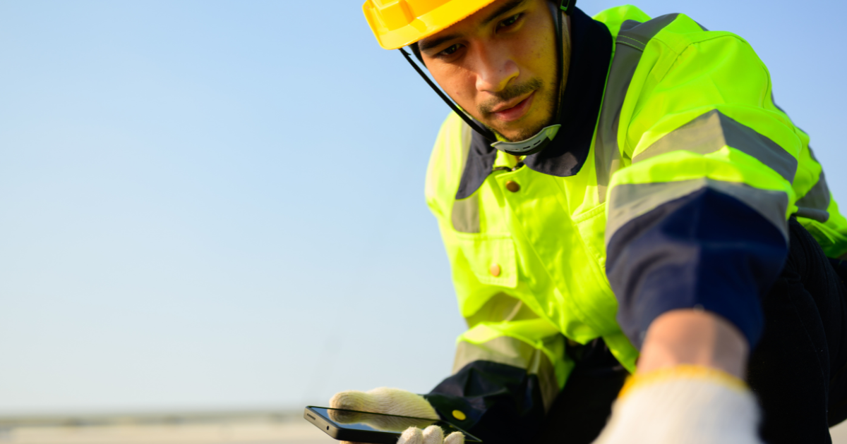 Person in high-visibility safety gear using a device on a clear day